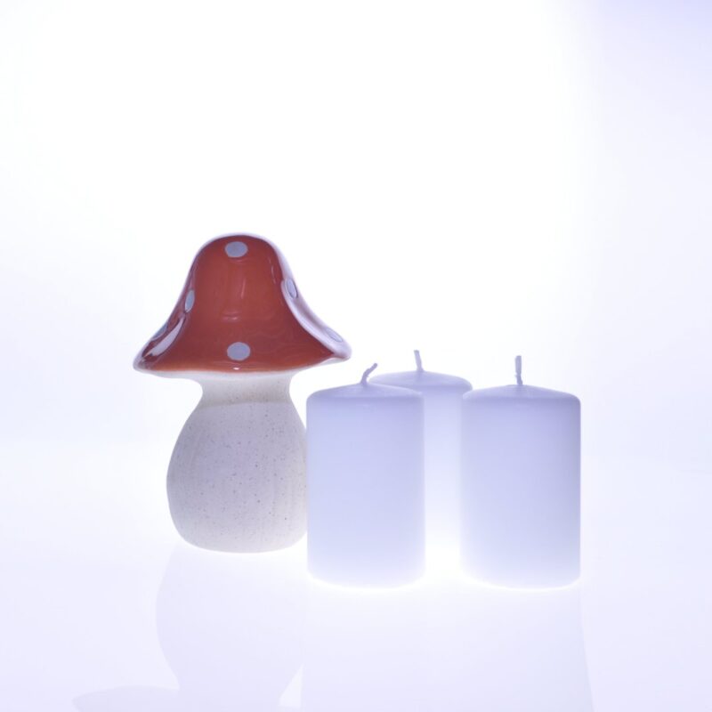 Zestaw trzech białych świec o gładkiej powierzchni ustawionych obok ceramicznej dekoracji w kształcie grzyba. Stylowa ozdoba idealna do wnętrz, dekoracji lub na prezent.